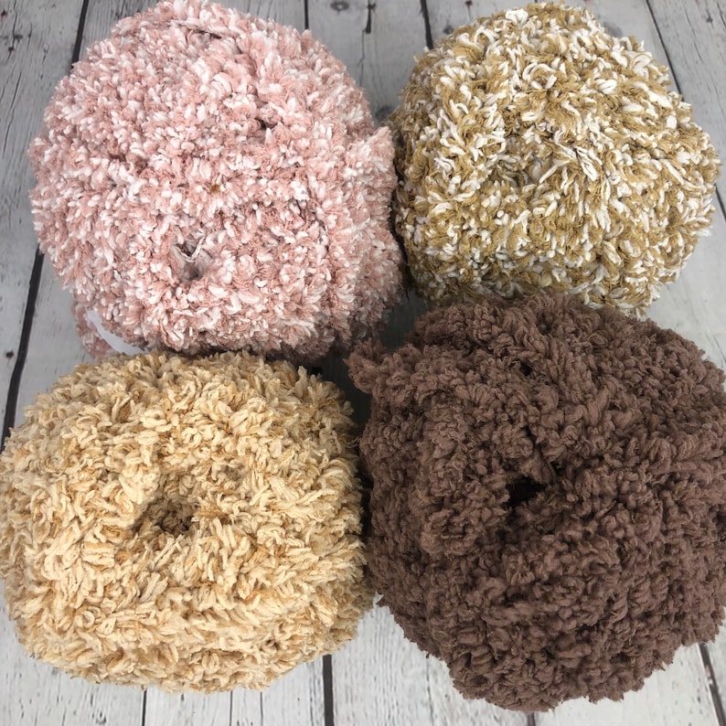 May include: Four balls of yarn in different colors: pink with white, beige with white, beige, and brown. The yarn is fluffy and textured.