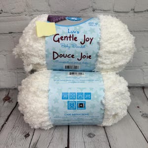 May include: Two white balls of yarn labeled "Luv's Gentle Joy Baby Blanket" and "Douce Joie Couverture pour bébé". The yarn is 200 grams and 200 meters. The label also includes care instructions for machine washing and drying.