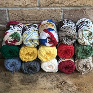 May include: A stack of 12 balls of yarn in various colors and patterns, including red, white, blue, green, yellow, and gray. The yarn is labeled "Sugar'n Cream" and "Peaches 'n Creme".
