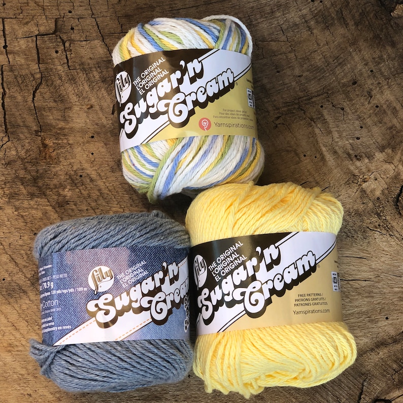 May include: Three skeins of Sugar'n Cream cotton yarn. One skein is yellow, one is blue, and one is a multi-colored mix of white, yellow, blue, and green.