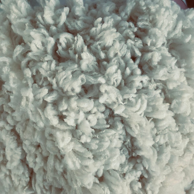 May include: Close-up of a fluffy, white, faux fur fabric. The texture is soft and plush, resembling a sheepskin.