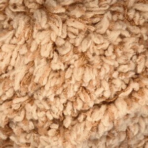 May include: Close-up of a soft, fluffy, beige and brown faux fur fabric. The fabric has a textured, curly, and fuzzy appearance.
