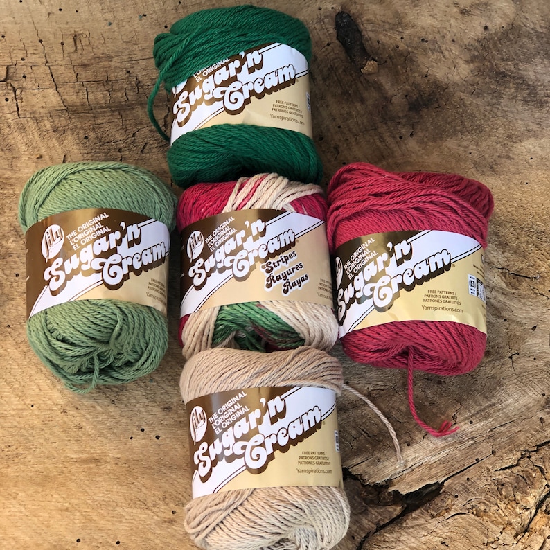 May include: Five spools of Sugar'n Cream yarn in green, white and red stripes, beige, and red. The yarn is labeled "The Original Sugar'n Cream" with the brand name "Lily".
