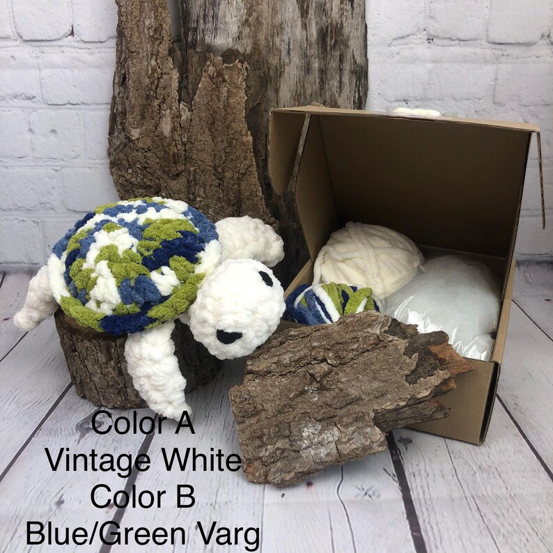 May include: A crochet turtle kit featuring a plush white and blue-green variegated yarn turtle, a cardboard box containing white yarn and stuffing, and text reading Color A Vintage White and Color B Blue/Green Varg.