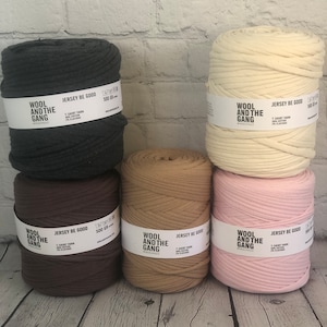 May include: Five spools of yarn in different colors: charcoal gray, brown, beige, pink, and cream. Each spool has a label that reads "Wool and the Gang" and "Jersey Be Good".