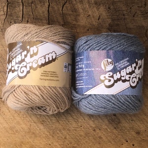 May include: Two skeins of Sugar'n Cream yarn, one in beige and one in blue. The label reads "The Original L'Original El Original Sugar'n Cream" and includes free patterns.