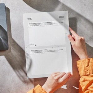 May include: A white paper worksheet titled Chapter 1: The Why and Disorderly Adventure, featuring two large blank rectangular boxes for writing. The text includes questions about moving to a new place, with a small airplane icon and a dashed flight path.