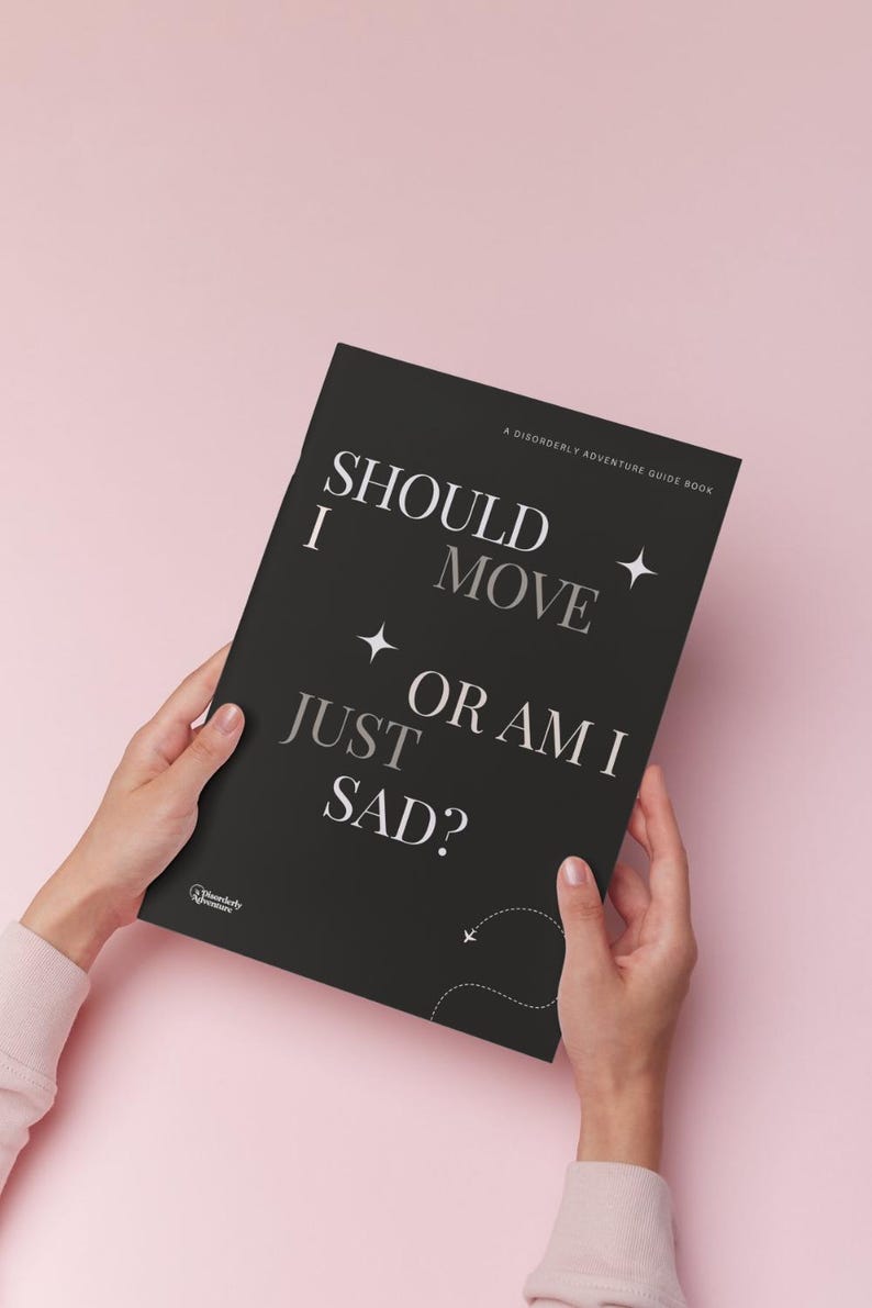 May include: A black rectangular guidebook with white text that reads SHOULD I MOVE OR AM I JUST SAD? and A DISORDERLY ADVENTURE GUIDE BOOK. The cover features small white star icons and a dashed line path with a tiny airplane icon at the bottom.