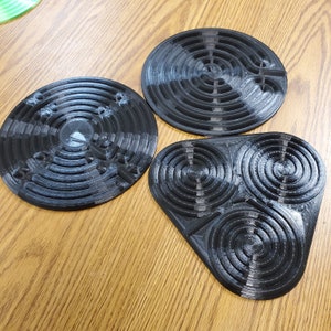 May include: Three black circular and triangular coasters with intricate maze-like designs. The coasters are made of a smooth, hard material.