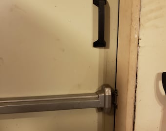 May include: A silver door handle with a black push bar and a black handle. The door handle is mounted on a white door.