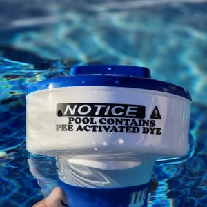 May include: White plastic pool alarm with blue trim. The alarm has a warning sign that reads "NOTICE POOL CONTAINS PEE ACTIVATED DYE".
