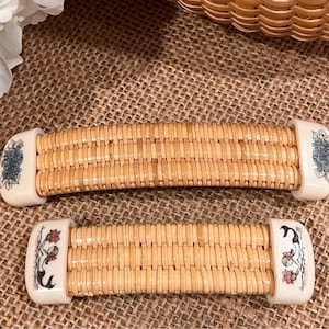 May include: Two woven wicker handles with white ceramic ends. The ends are decorated with floral designs. One handle has a blue flower design and the other has a red and green floral design.