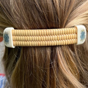 May include: A woven hair clip with a light brown wicker design and white floral accents. The clip is made of natural materials and has a simple, elegant design.