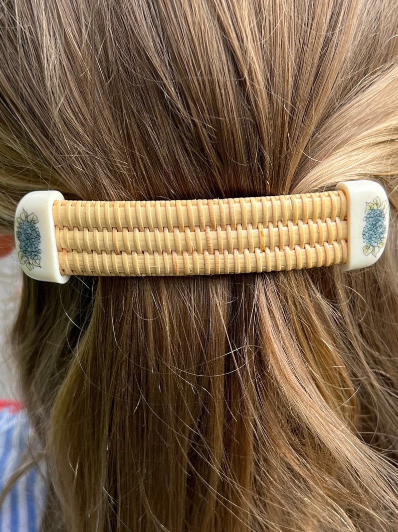 May include: A woven hair clip with a light brown wicker design and white floral accents. The clip is made of natural materials and has a simple, elegant design.