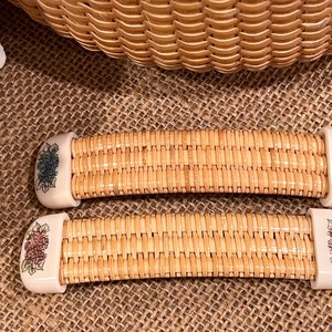 May include: Two woven wicker handles with floral designs. The handles are beige with white floral accents. One handle has blue flowers and the other has pink flowers.