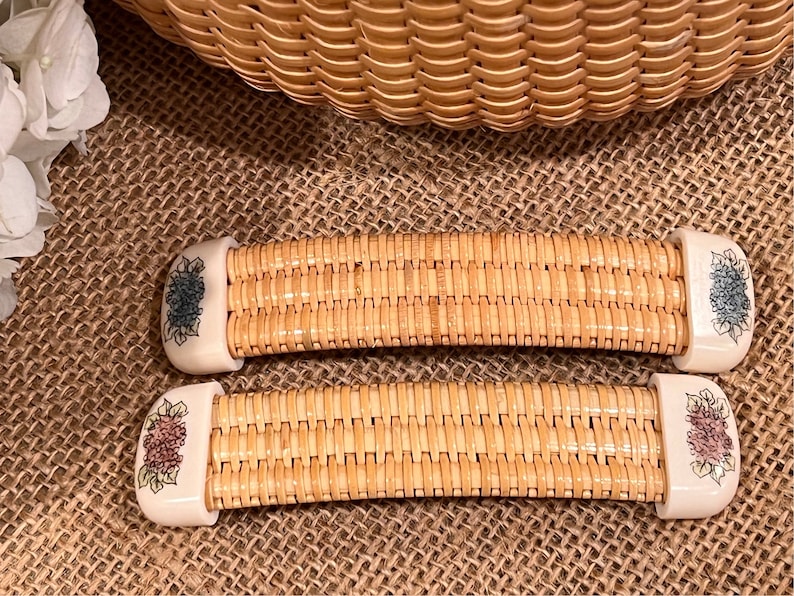May include: Two woven wicker handles with floral designs. The handles are beige with white floral accents. One handle has blue flowers and the other has pink flowers.