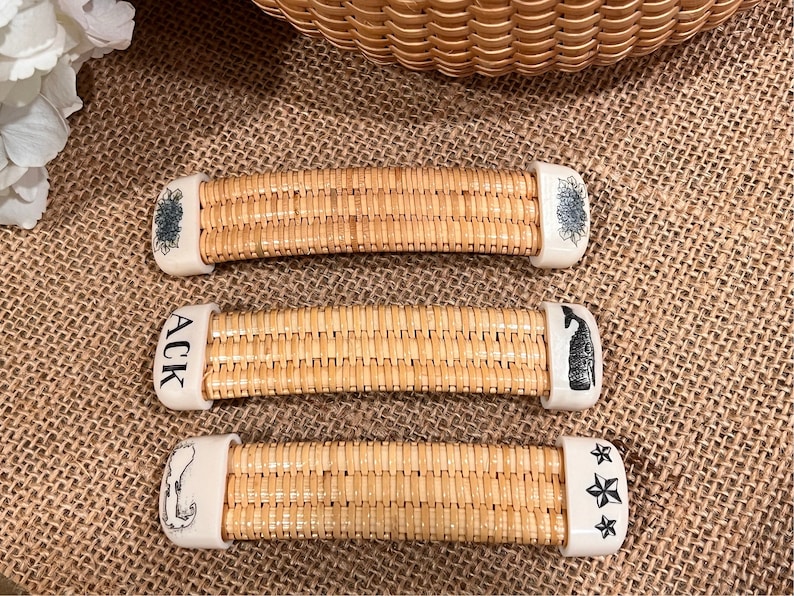 May include: Three wicker handles with white ceramic ends. The ends are decorated with different designs: a floral pattern, the letters "ACK", and a whale.