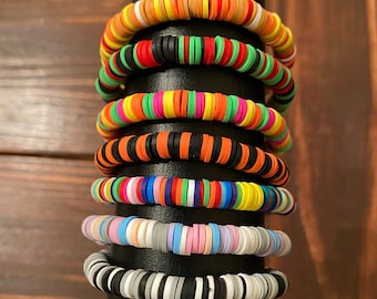 May include: A stack of colorful bracelets made of round beads. The bracelets are arranged in a vertical stack on a black stand. The bracelets are made of different colors, including orange, green, yellow, pink, blue, and white.