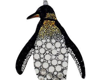 May include: A black and white penguin ornament with a yellow and orange chest. The penguin is painted with white and gray circles.
