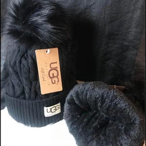 May include: Black knit beanie with a faux fur pom pom and a brown tag that says "UGG Australia Gift Card". The beanie has a black UGG logo on the side.