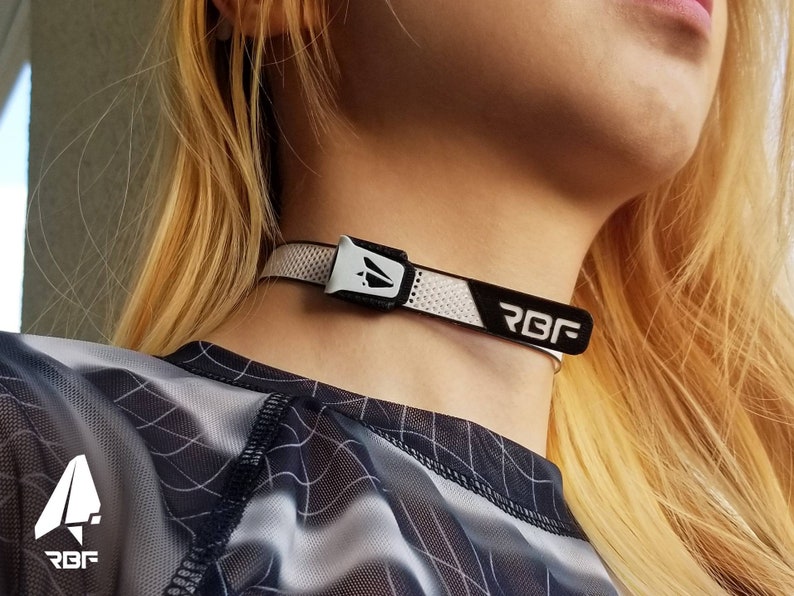 K&ouml;nnte beinhalten: Ein wei&szlig;-schwarzes Choker-Halsband mit den Buchstaben "RBF" darauf. Das Halsband hat ein Mesh-Design und einen silbernen Verschluss. Die Person auf dem Bild tr&auml;gt ein schwarz-wei&szlig; gemustertes Oberteil.
