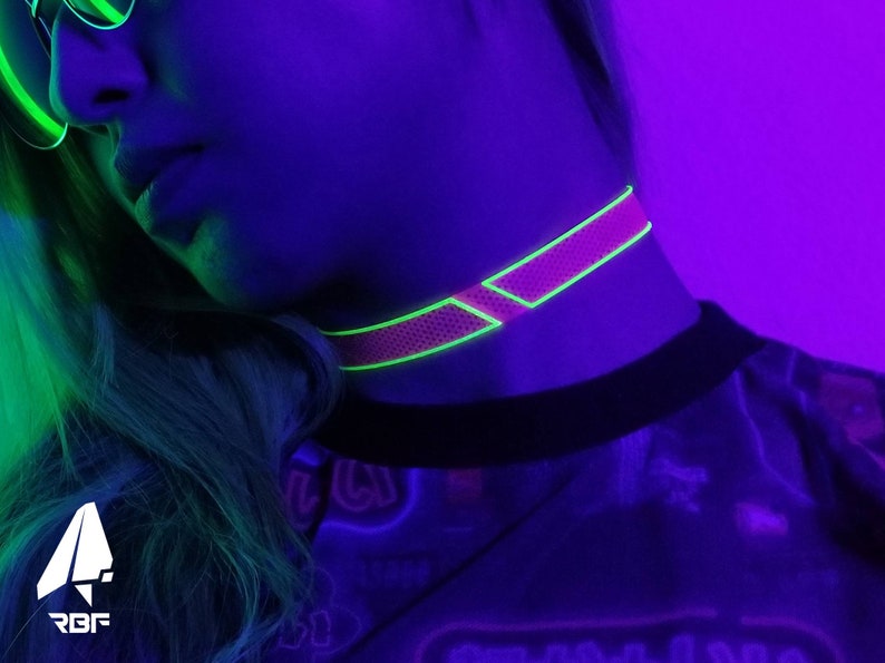 K&ouml;nnte beinhalten: Ein neonpinkfarbenes Choker-Halsband mit Mesh-Design und hellgr&uuml;ner Umrandung. Das Halsband wird um den Hals getragen. Das Bild ist mit neon-gr&uuml;nen und violetten Lichtern beleuchtet. Das RBF-Logo befindet sich in der unteren linken Ecke.