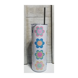 Pu&ograve; includere: Un bicchiere bianco isolato con una cannuccia nera. Il bicchiere &egrave; decorato con un motivo ripetuto di fiori sorridenti colorati nelle tonalit&agrave; del rosa, blu, verde e giallo. Il bicchiere &egrave; alto circa 23 cm.
