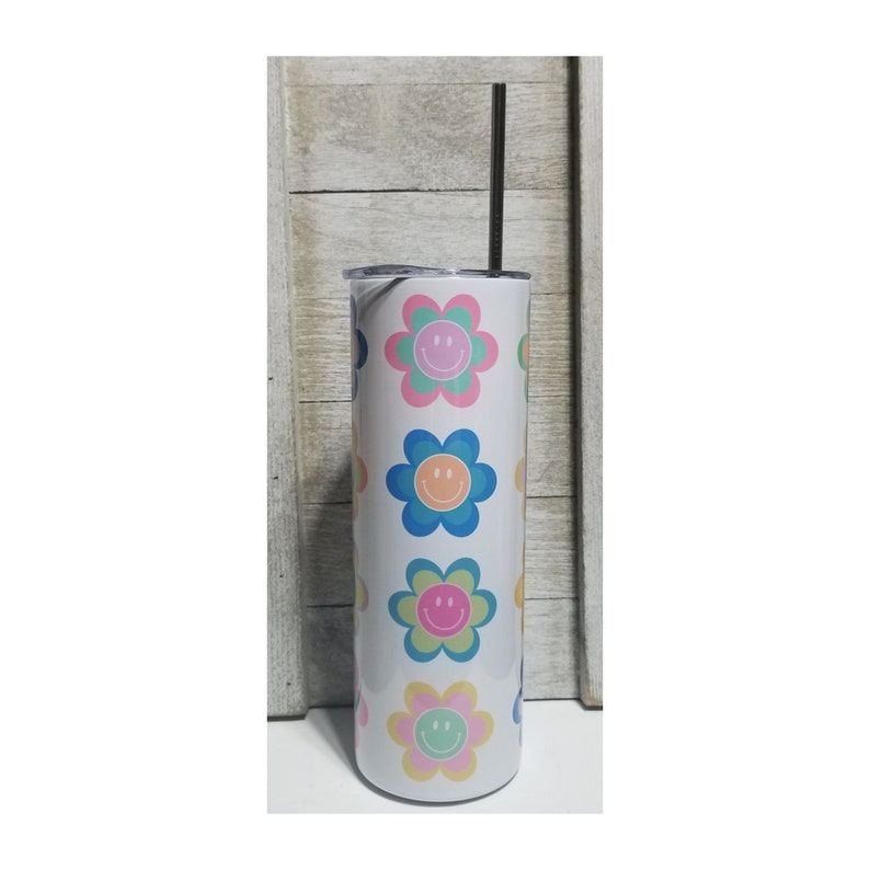 Pu&ograve; includere: Un bicchiere bianco isolato con una cannuccia nera. Il bicchiere &egrave; decorato con un motivo ripetuto di fiori sorridenti colorati nelle tonalit&agrave; del rosa, blu, verde e giallo. Il bicchiere &egrave; alto circa 23 cm.