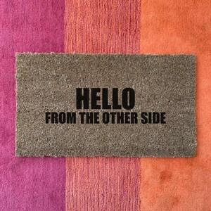 May include: A brown doormat with the text "HELLO FROM THE OTHER SIDE" in black lettering.