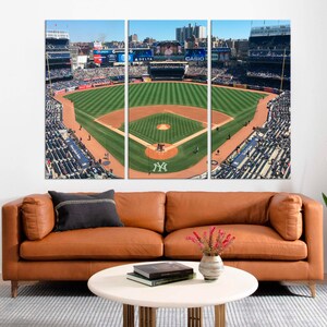 May include: An aerial view of a baseball field with a green grass infield and a brown dirt outfield. The stands are full of fans wearing blue and white clothing. The field is surrounded by a fence and there are several signs visible, including "DELTA" and "CASIO".