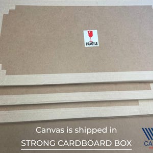 May include: Stacked, rectangular cardboard boxes with white edges and a brown interior. A red and white "Fragile" sticker is visible on the top box. The text "Canvas is shipped in STRONG CARDBOARD BOX" is printed on the bottom.