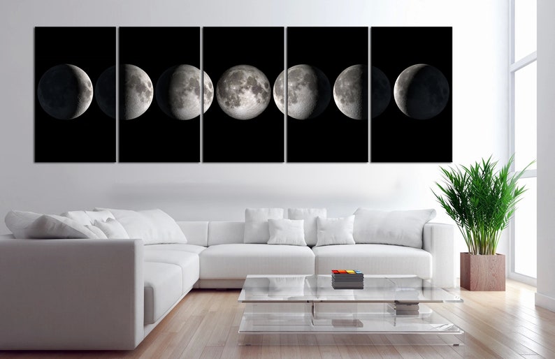 May include: A black and white canvas print of the moon in different phases. The print is divided into eight sections, each showing a different phase of the moon. The print is hanging on a white wall above a white couch and a glass coffee table.