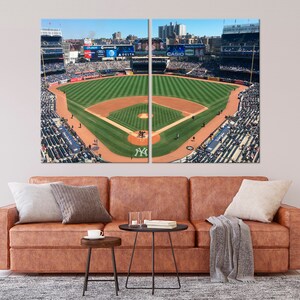 May include: An aerial view of a baseball field with a green grass infield and a brown dirt outfield. The stands are full of fans wearing blue and white clothing. The scoreboard displays the names of sponsors, including "Delta" and "Casio".
