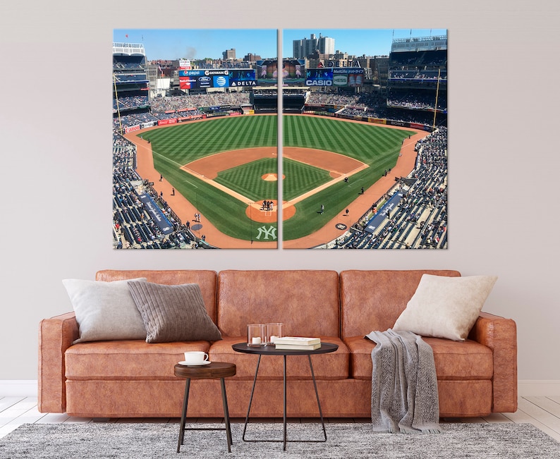 May include: An aerial view of a baseball field with a green grass infield and a brown dirt outfield. The stands are full of fans wearing blue and white clothing. The scoreboard displays the names of sponsors, including "Delta" and "Casio".