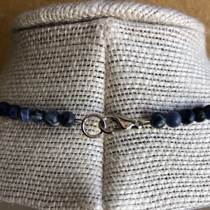 May include: A close-up of a silver clasp on a necklace made of dark blue gemstone beads.