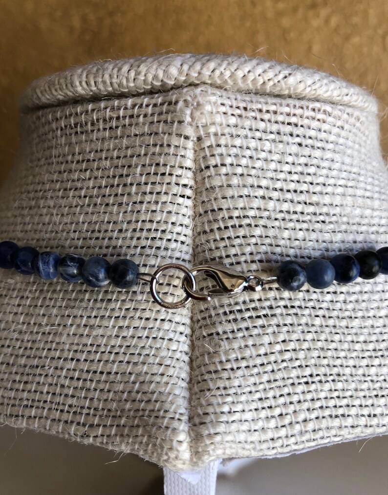 May include: A close-up of a silver clasp on a necklace made of dark blue gemstone beads.