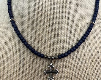 May include: A black beaded necklace with a silver cross pendant.