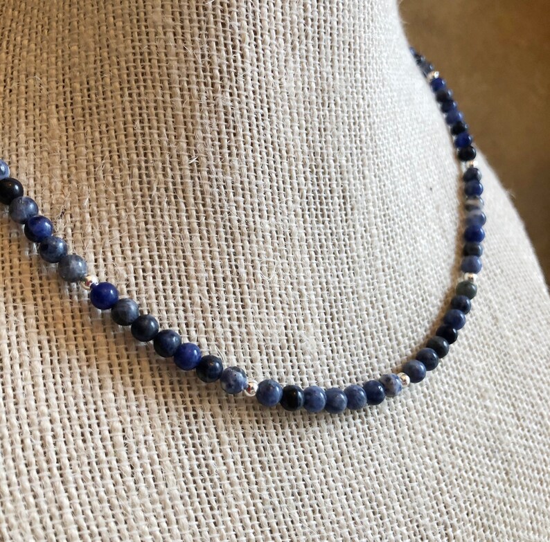 May include: A blue and black gemstone necklace with silver beads. The necklace is made of small, round beads that are strung together on a silver chain.