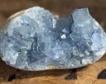 May include: A blue celestite crystal cluster with a rough, natural exterior and a smooth, polished interior. The crystal is filled with many small, sparkling crystals.
