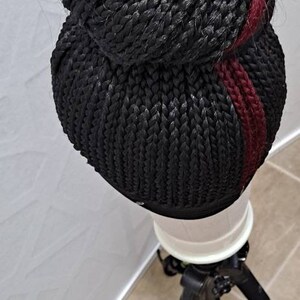 Pu&ograve; includere: Parrucca intrecciata nera con una striscia bordeaux. La parrucca &egrave; acconciata a forma di chignon ed &egrave; esposta su un supporto bianco. La parrucca &egrave; realizzata con fibre sintetiche ed &egrave; progettata per essere indossata come acconciatura protettiva.