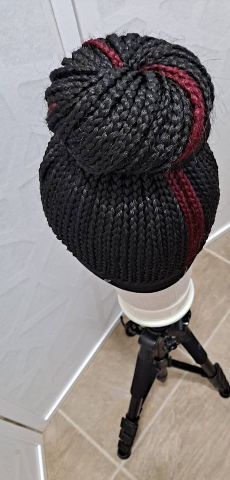 Pu&ograve; includere: Parrucca intrecciata nera con una striscia bordeaux. La parrucca &egrave; acconciata a forma di chignon ed &egrave; esposta su un supporto bianco. La parrucca &egrave; realizzata con fibre sintetiche ed &egrave; progettata per essere indossata come acconciatura protettiva.