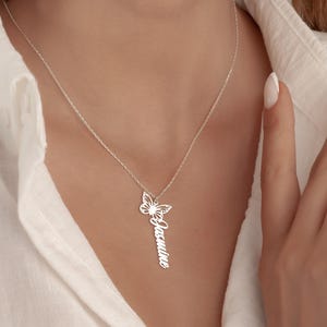 May include: A silver necklace with a butterfly pendant and a vertical nameplate. The butterfly design is detailed, and the name "Jasmine" is inscribed. The necklace is shown against a white shirt.