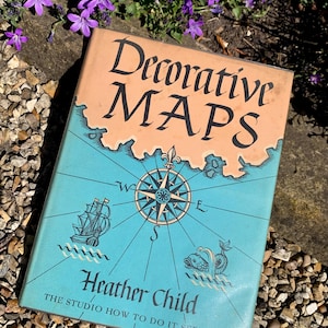 May include: A vintage book titled "Decorative Maps" with a teal and orange cover. The cover features a compass rose, a ship, and a sea creature illustration. The author's name, Heather Child, is also visible.