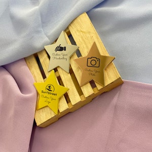 May include: Three star-shaped metal pins in gold, silver, and bronze tones, each with a unique design. One pin features a camera icon and the text "Custom Your Photo." Another has a pen icon and the text "Custom Your Handwriting." The third pin has a logo and the text "Custom Your Logo."