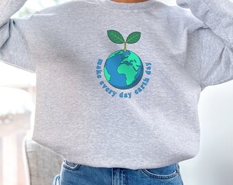 Puede incluir: Sudadera gris con una planta verde que crece de un globo terráqueo azul. El texto "make every day earth day" está escrito alrededor del globo.