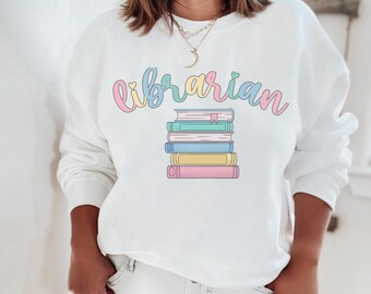 Peut inclure: Sweat-shirt blanc avec le texte "bibliothécaire" en couleurs pastel et une pile de livres avec un cœur sur le livre du dessus.