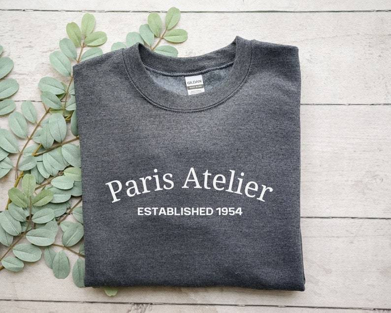May include: A dark gray sweatshirt with the text "Paris Atelier Established 1954" printed in white.