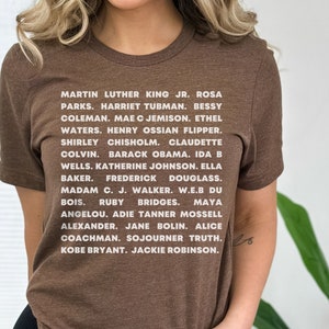 Może przedstawiać: Brązowa koszulka z białym tekstem, na którym wymienione są nazwiska wybitnych Afroamerykanów, w tym Martina Luthera Kinga Jr., Rosy Parks, Harriet Tubman i wielu innych.