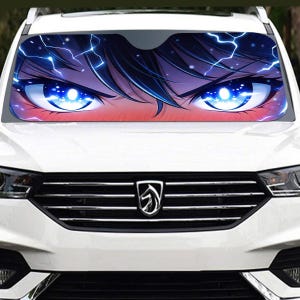 May include: A white car with a windshield sunshade featuring a close-up of anime-style eyes. The eyes are bright blue with lightning bolt accents and dark blue hair. The sunshade is a car accessory.