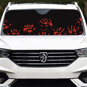 May include: Black car windshield sunshade with a graphic of red handprints and dripping blood. The sunshade is designed to fit a car's windshield and protect the interior from sunlight.